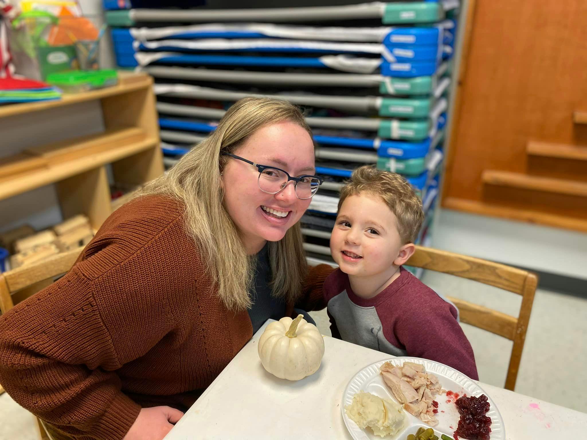 Person and child sitting at a table with a plate of food and a small pumpkin