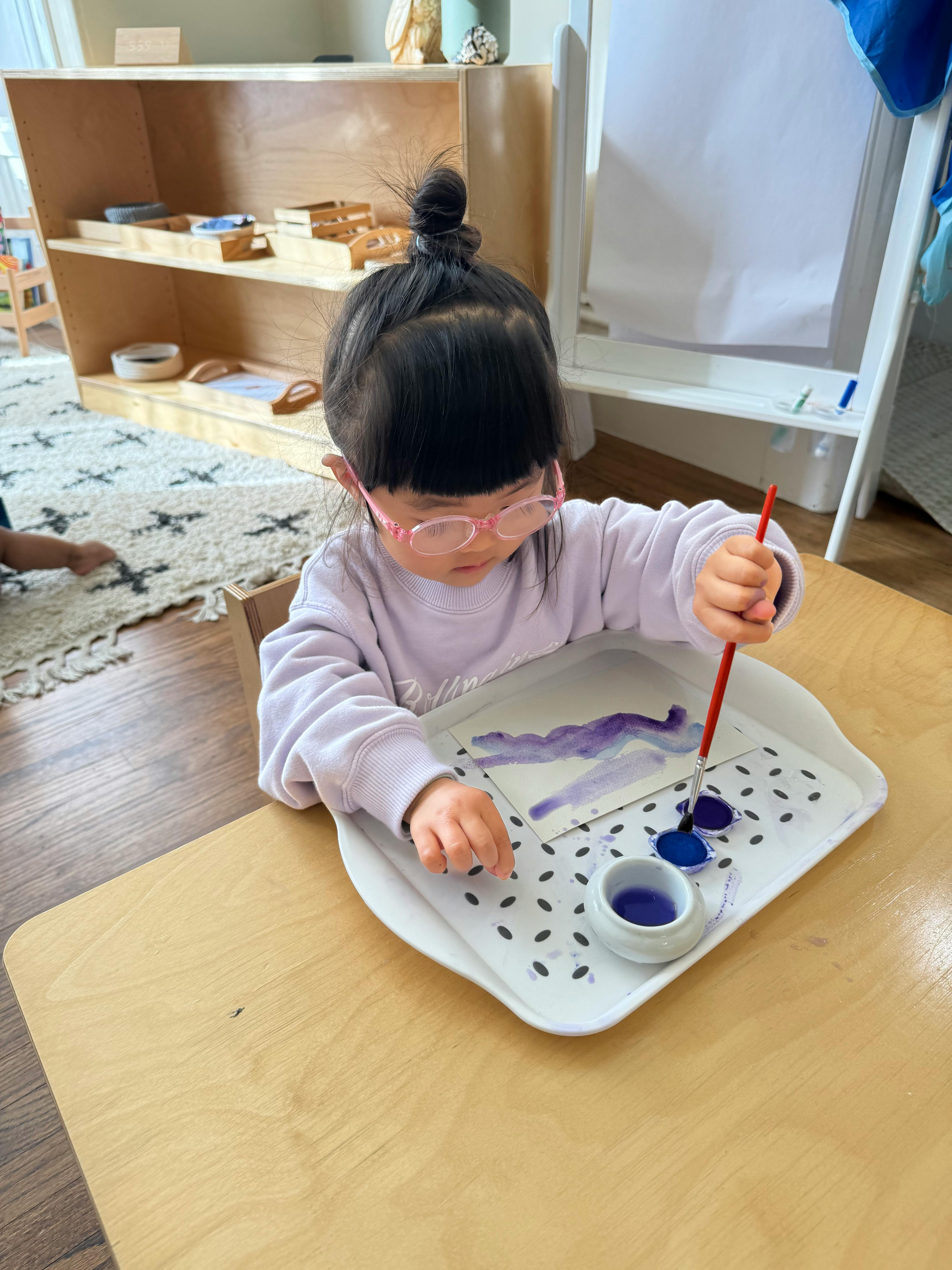 Child painting with purple watercolor on a tray