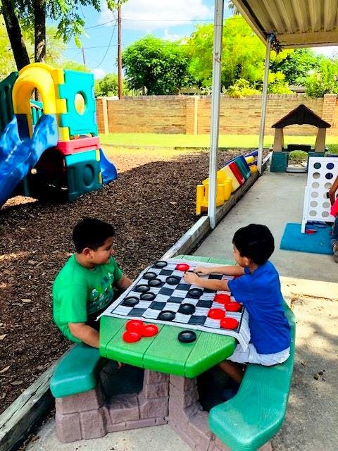 Two children playing checkers at a green picnic table outdoors