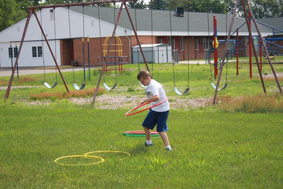 Child playing with a hula hoop on a grassy playground