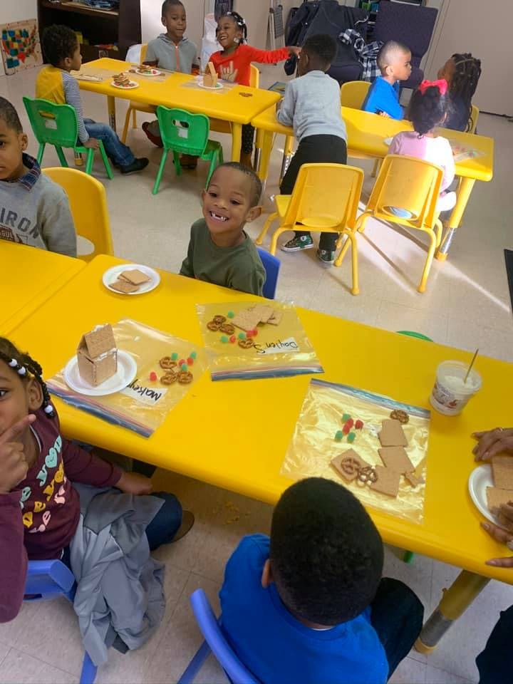 Children sitting at yellow tables with gingerbread house kits