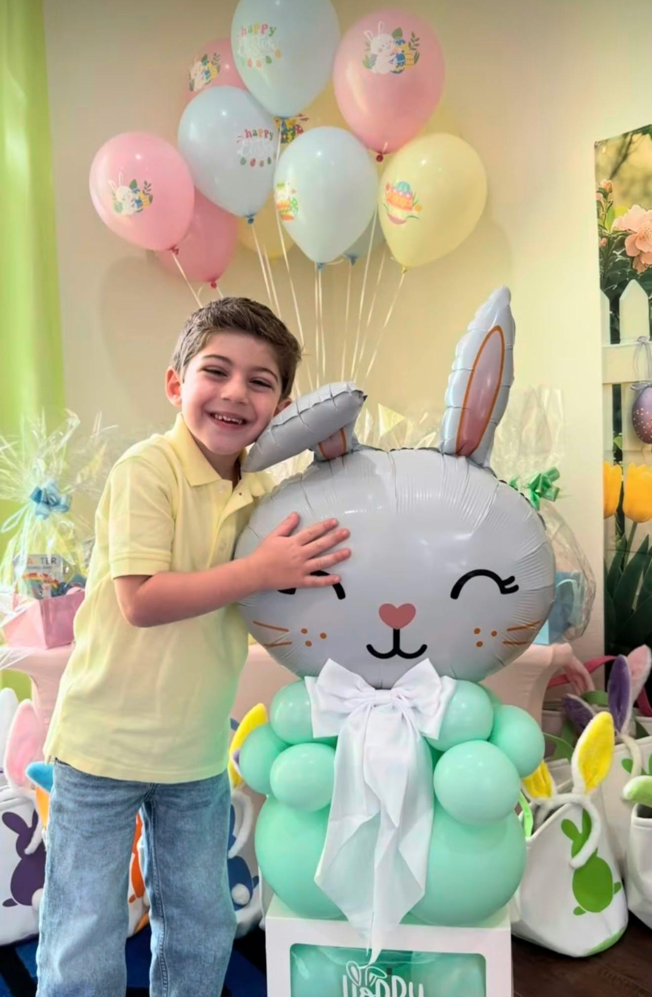 Child hugging a large Easter bunny balloon with pastel balloon decorations