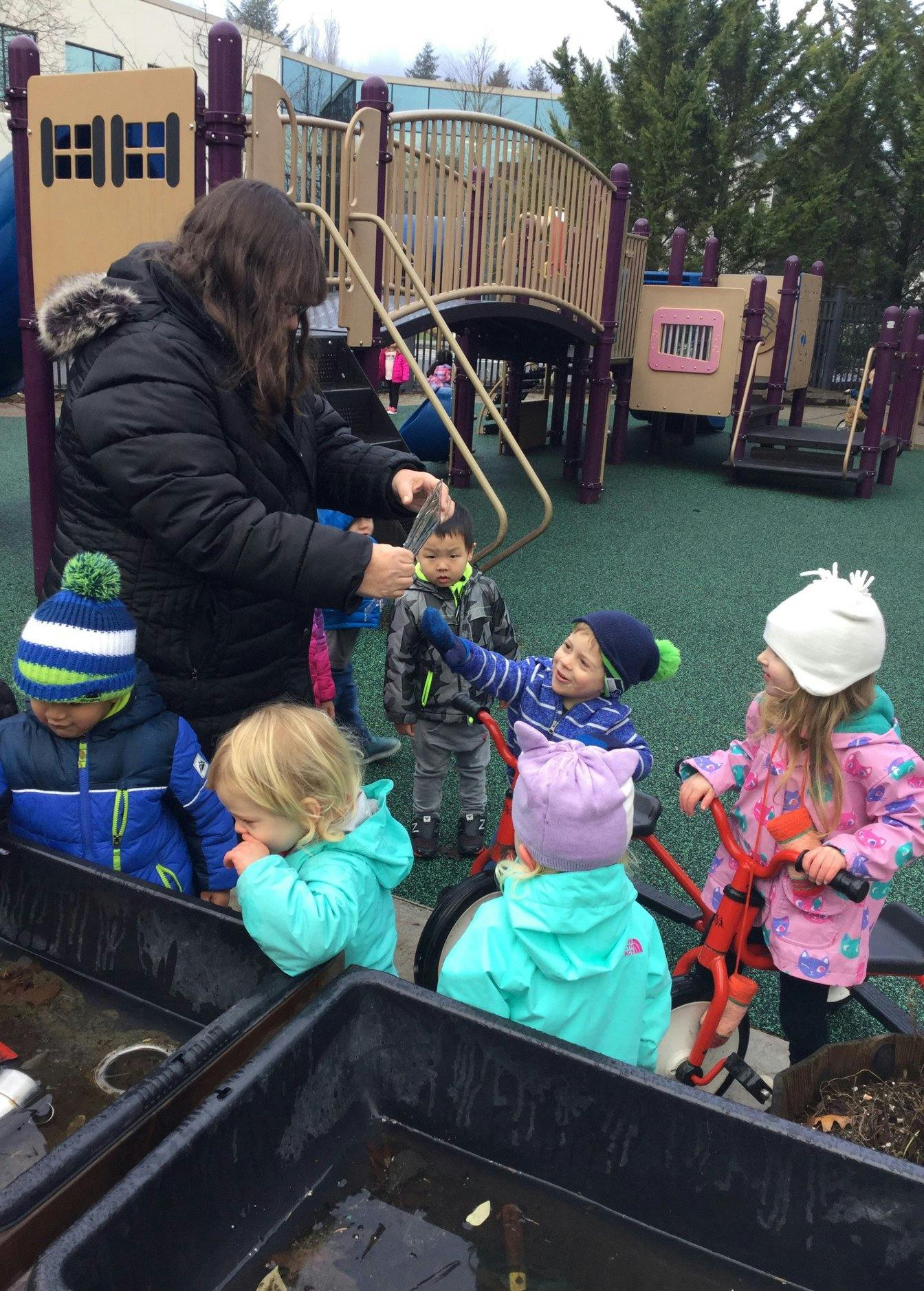 Adult and children playing with water and dirt in a playground