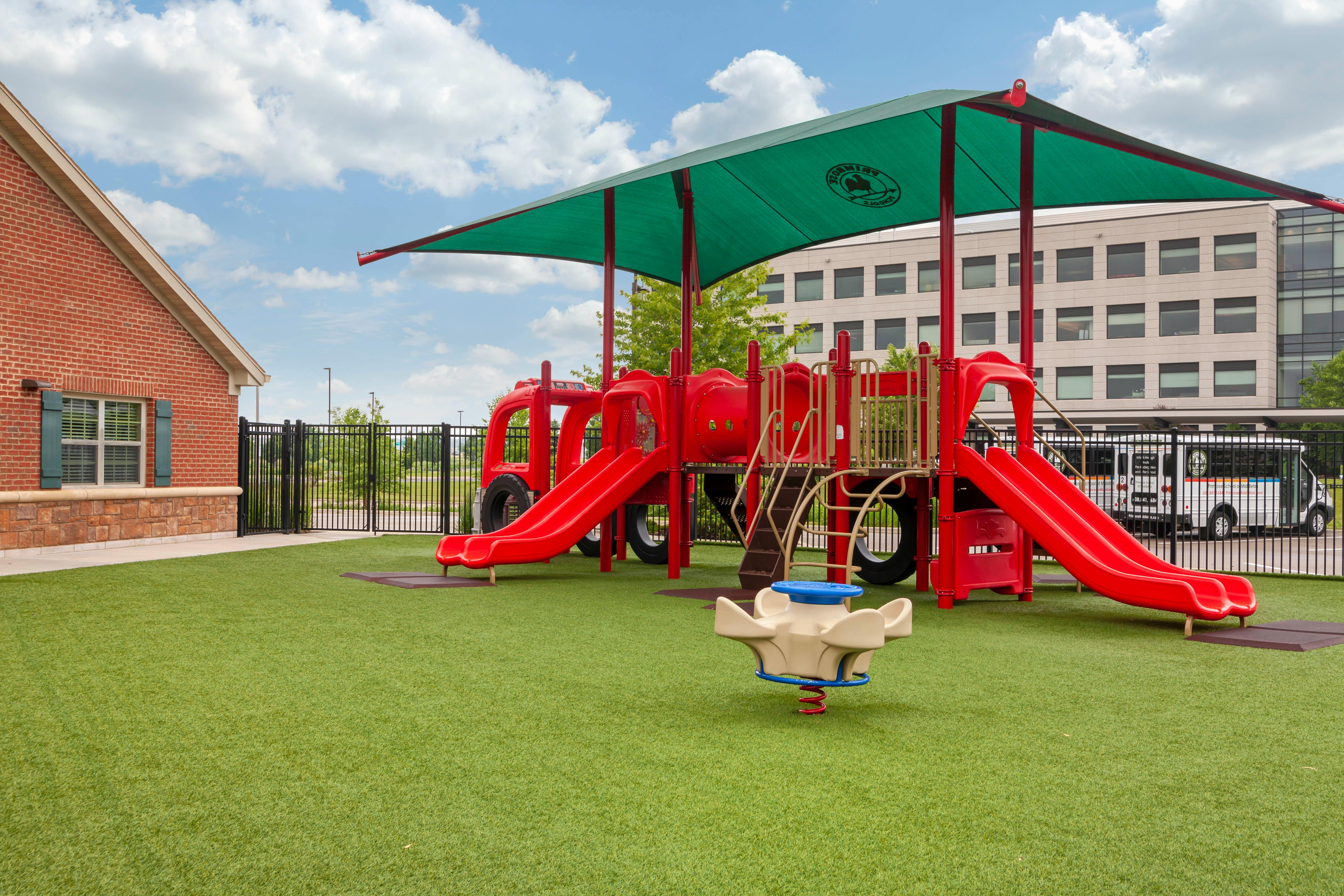 Red playground with slides and a green sunshade on artificial turf