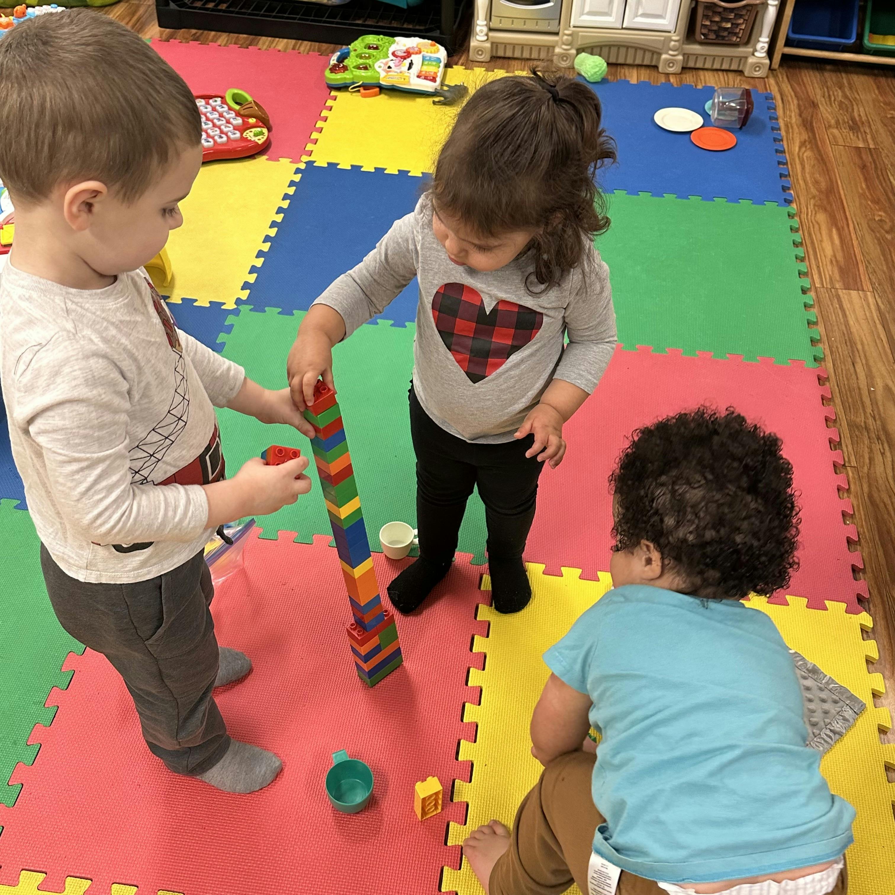 Three children playing with colorful building blocks on a mat