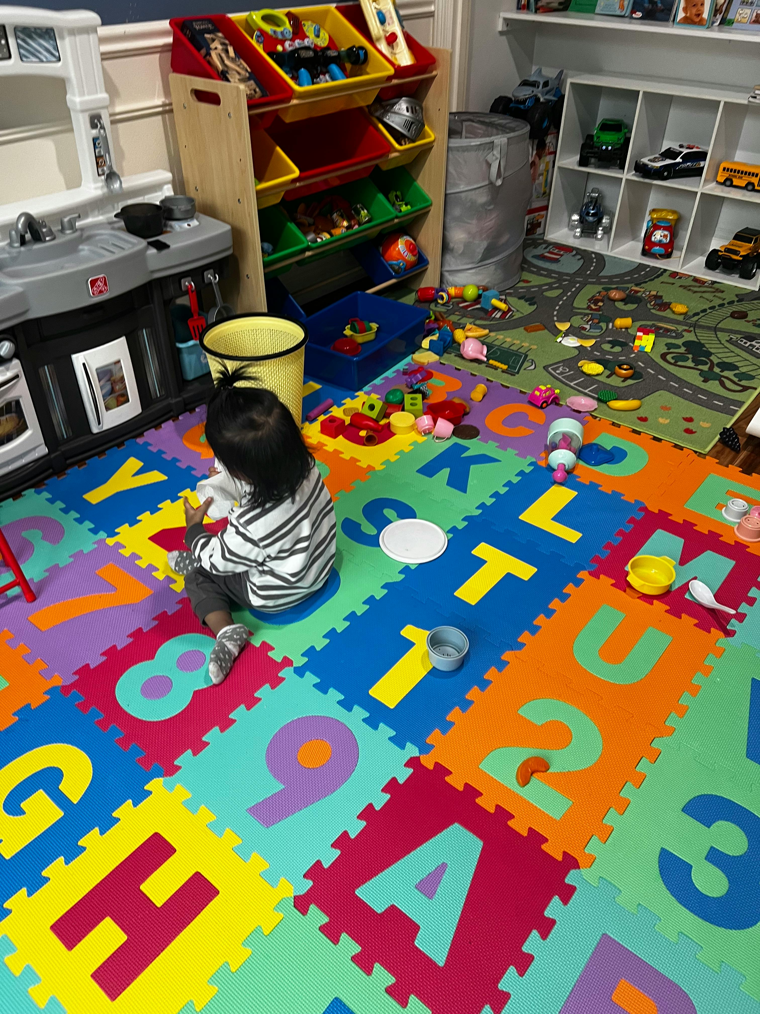 Child sitting on alphabet playmat with toys