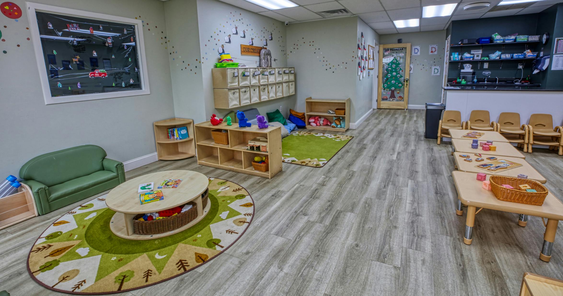 A childcare classroom with tables and chairs, shelves, couches, and play rugs