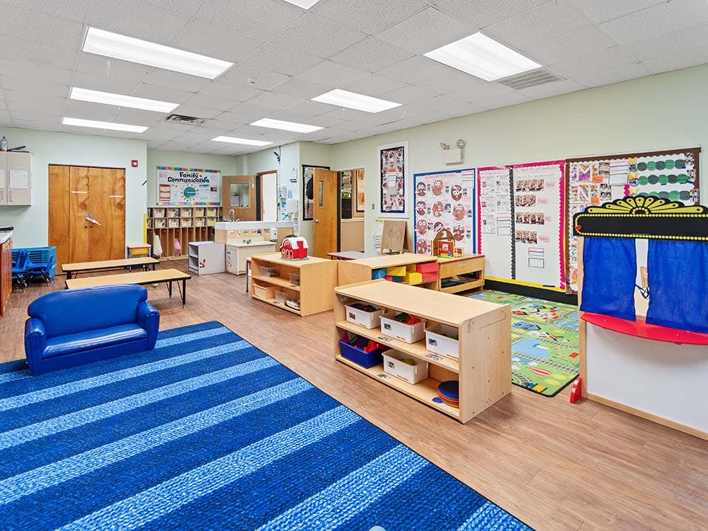 An empty early childhood classroom with a blue striped rug and various play areas