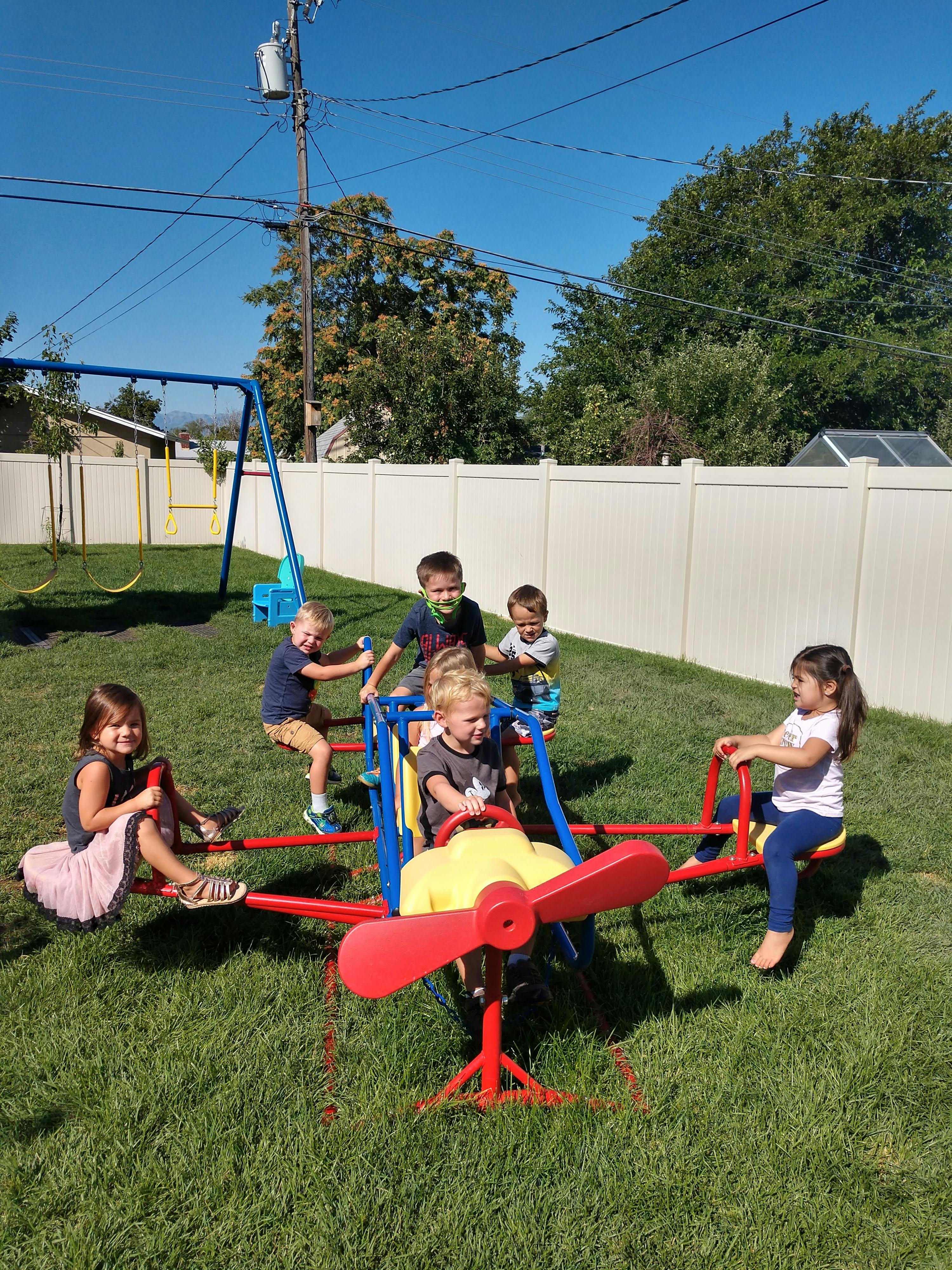 Children playing on a seesaw and a swing set in a grassy yard