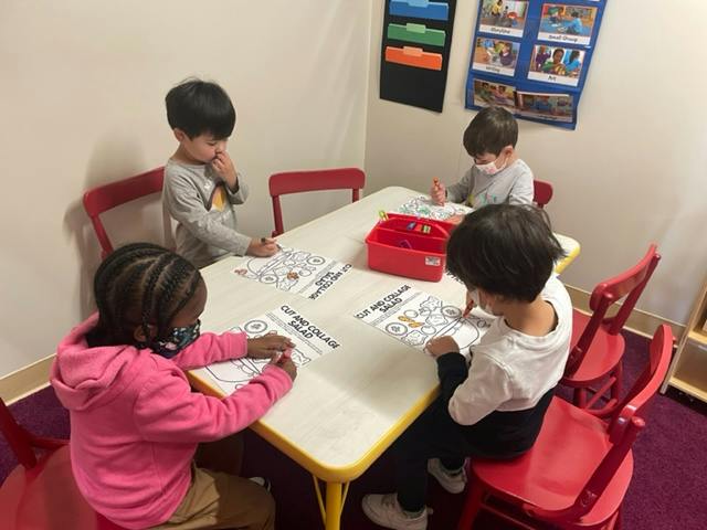 Four children sitting at a table coloring in a classroom, coloring