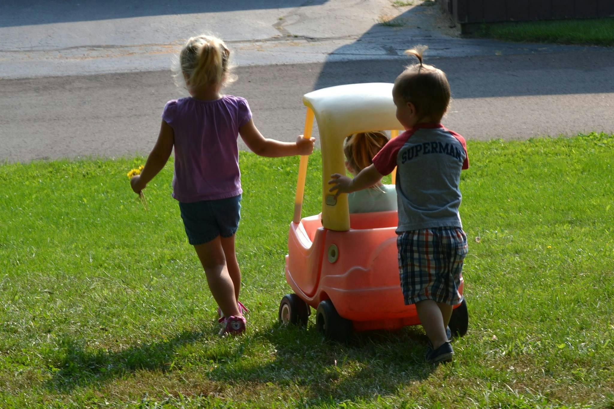 Two children playing with a toy car on grass