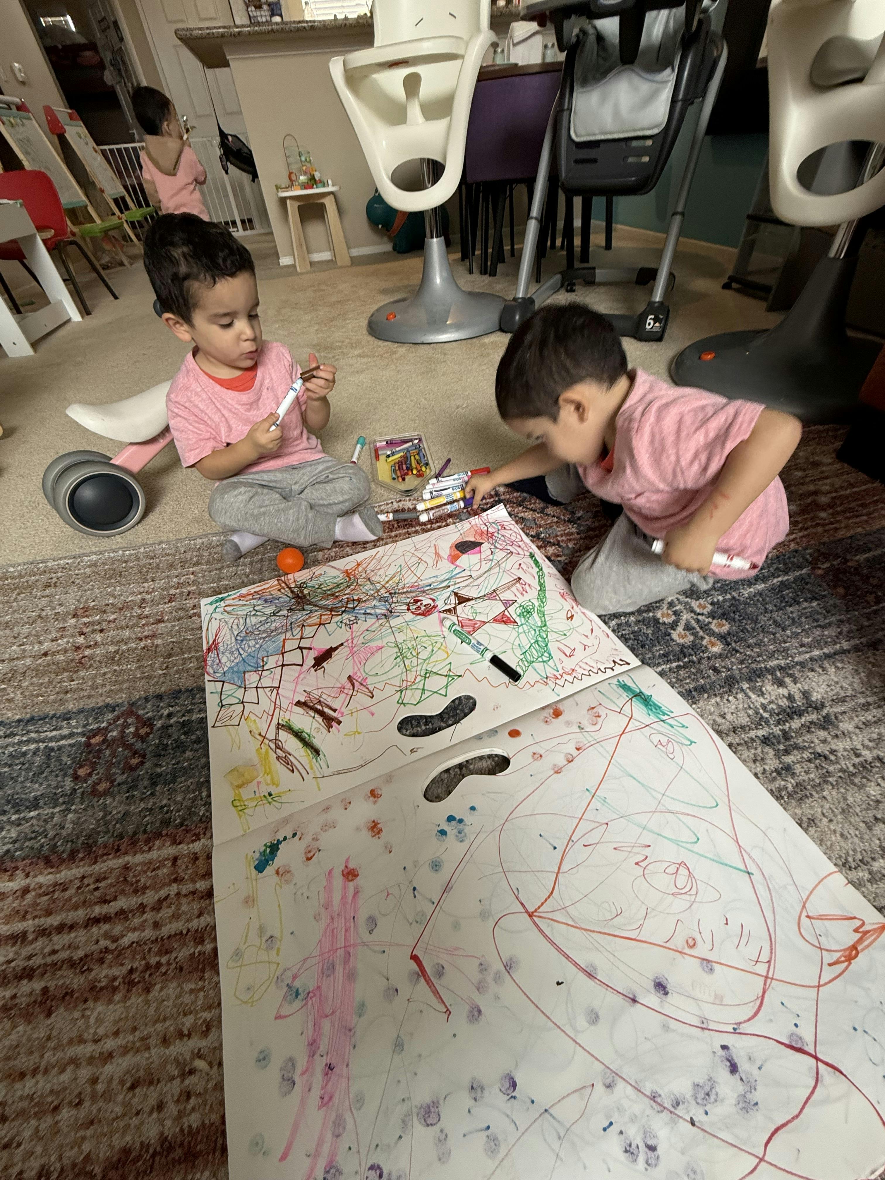 Two children drawing with markers on a large sheet of paper on the floor