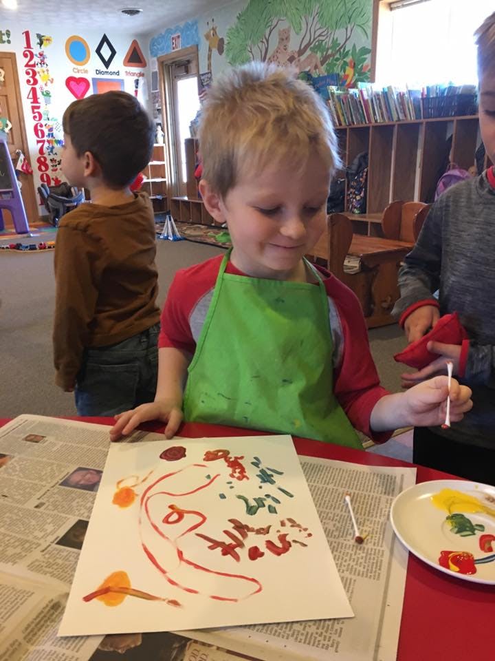 Child in green apron painting with a cotton swab