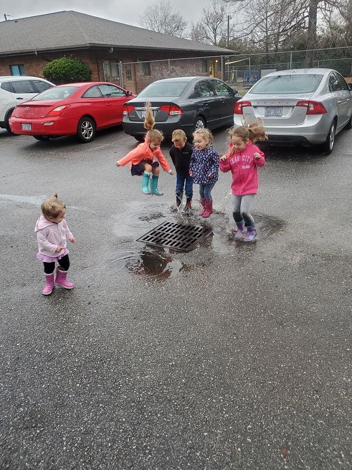 Children in rain boots playing in puddles near a storm drain