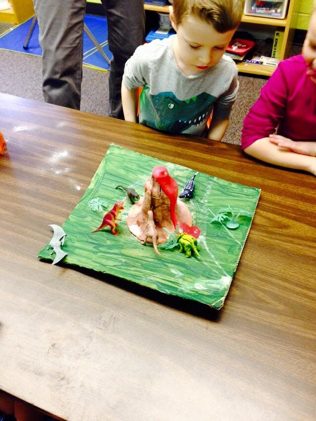Child looking at a volcano model with toy dinosaurs