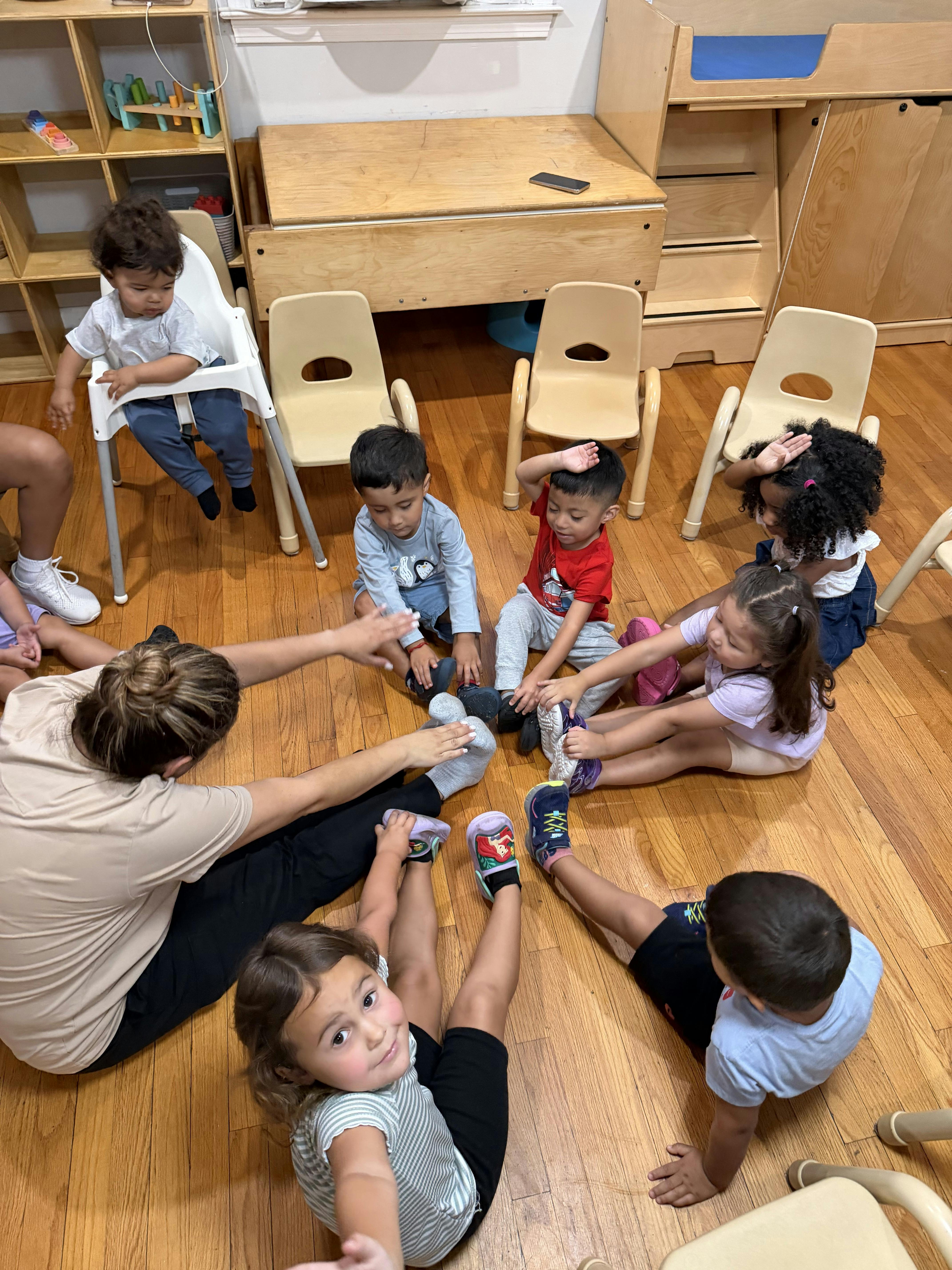 Group of children and a teacher sitting on the floor stretching in a circle