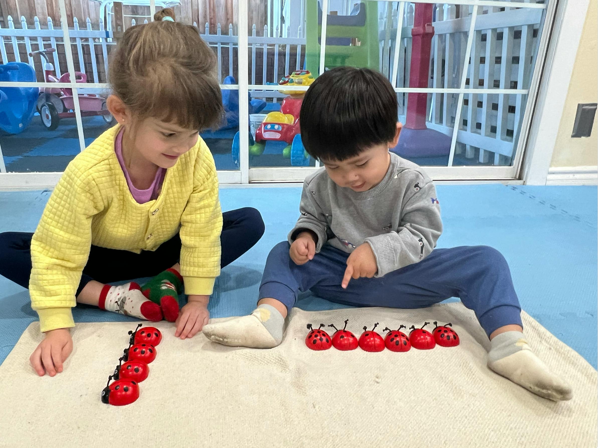 Two children sitting on the floor, playing with ladybug counting toys