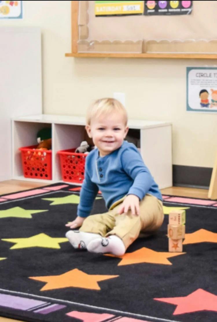 Child sitting on a star-patterned rug with wooden blocks in a classroom