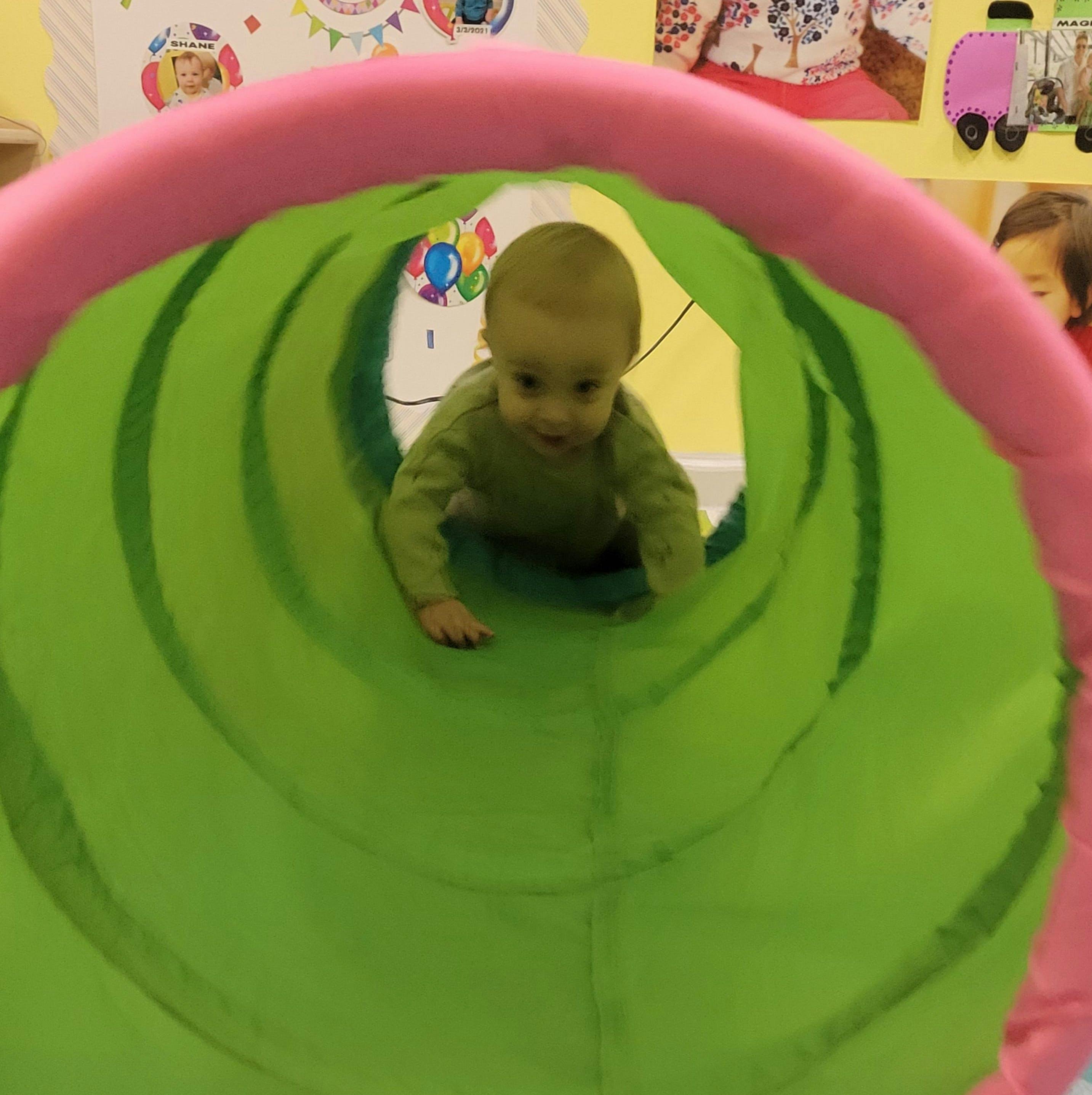 Child crawling through a green and pink play tunnel