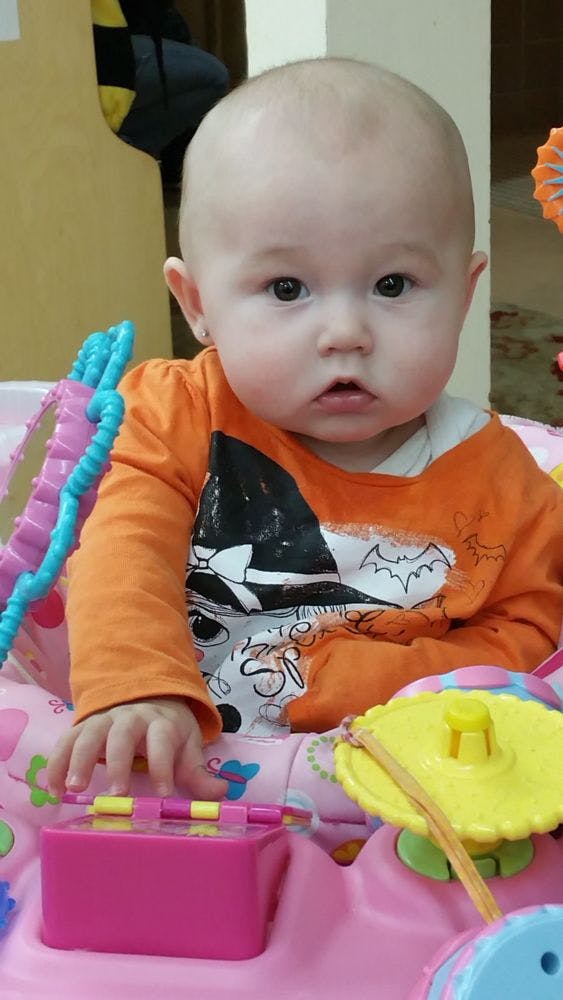 Child in an orange shirt sitting in a pink activity center