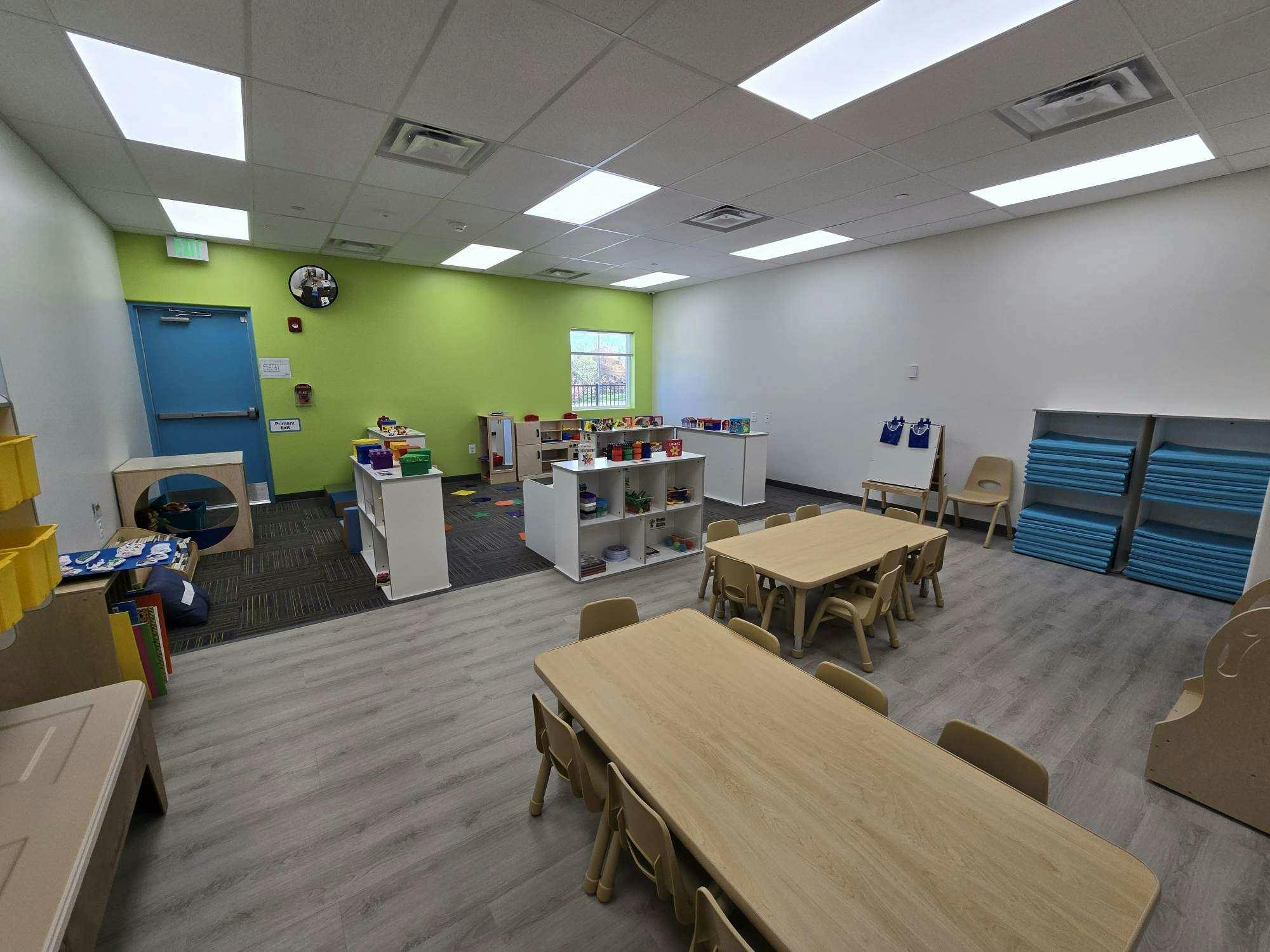 Classroom with small tables and chairs, shelves, and a green accent wall