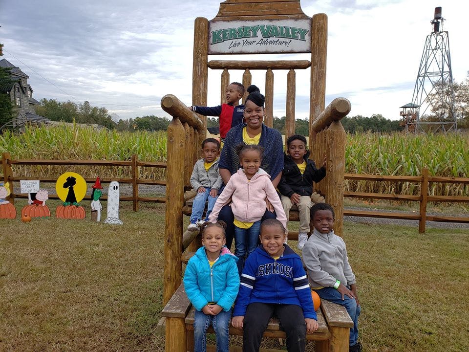 Adult and children sitting on a large wooden chair with "Kersey Valley" sign