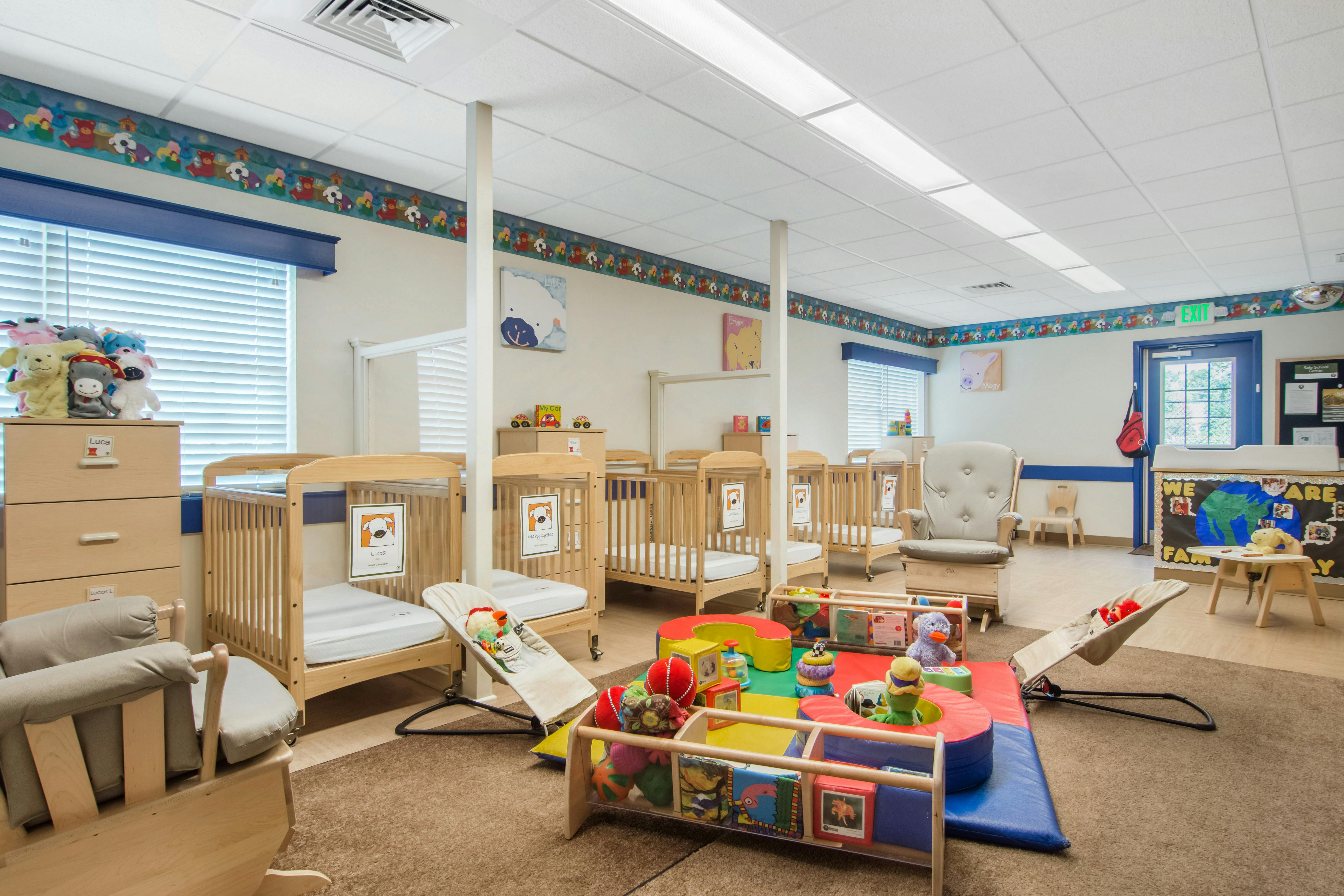 Cribs, infant bouncers, and play area in a daycare room