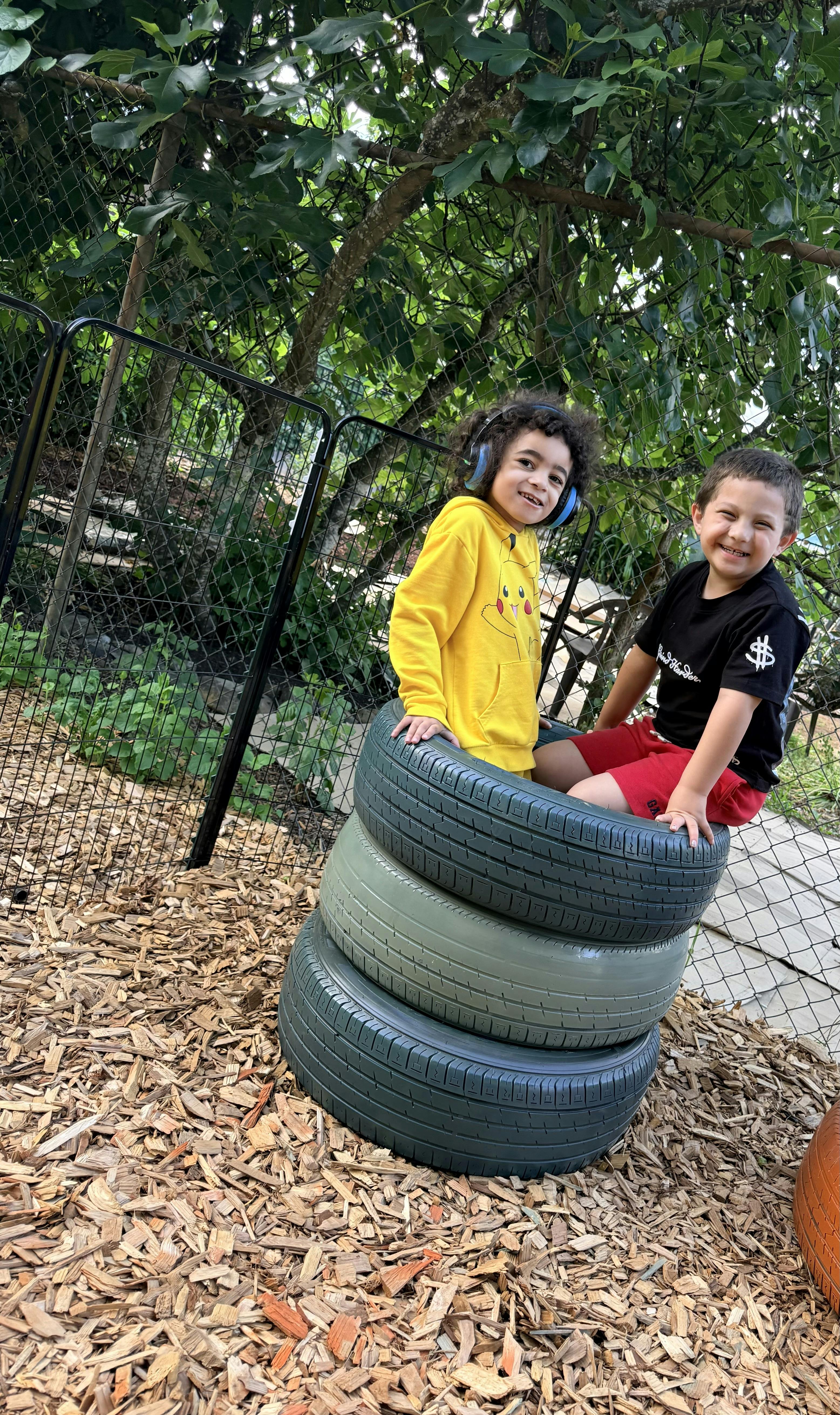 Two children sitting on stacked tires on a wood chip playground