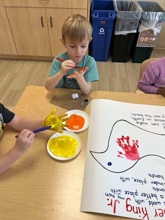Child painting their hand orange in a classroom
