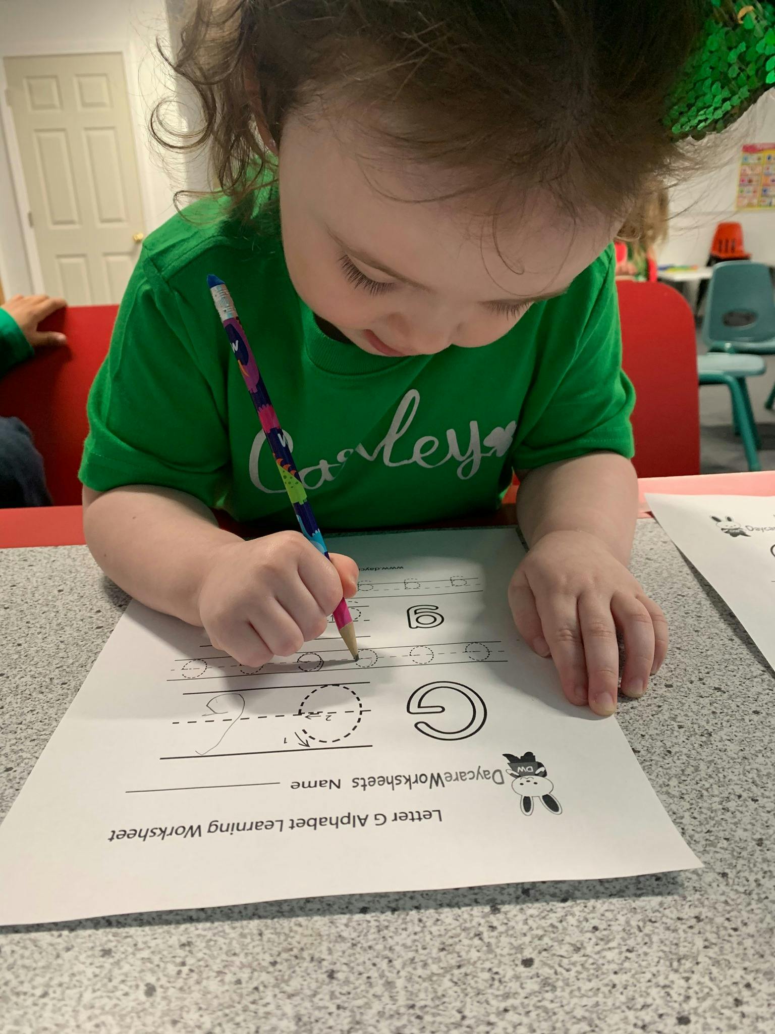 Child writing on a letter G alphabet learning worksheet