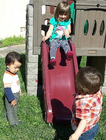 Child on a slide with two other children nearby