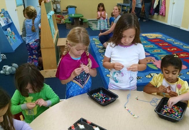 Children making beaded jewelry at a table in a classroom