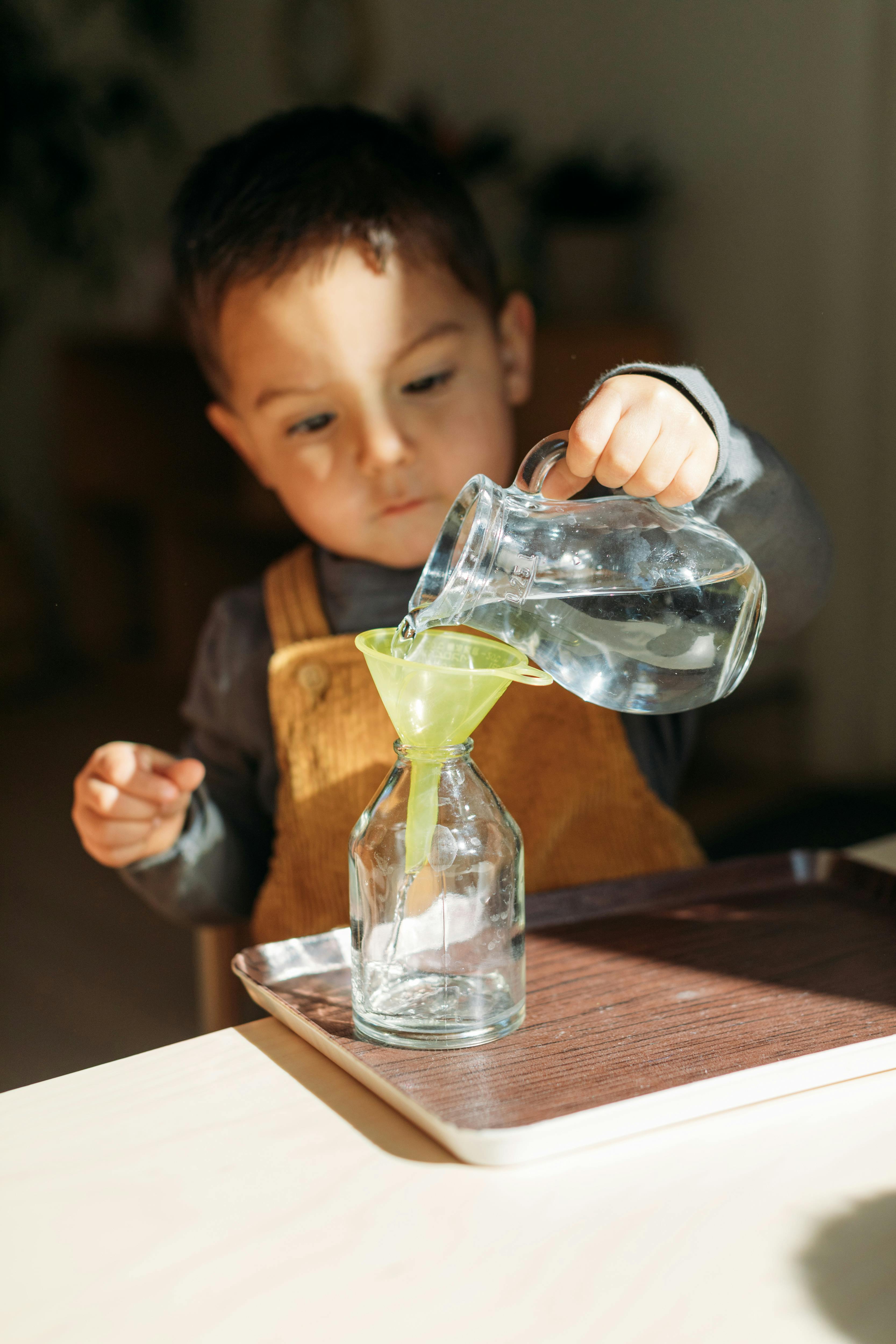 Child pouring water from a pitcher into a bottle using a funnel