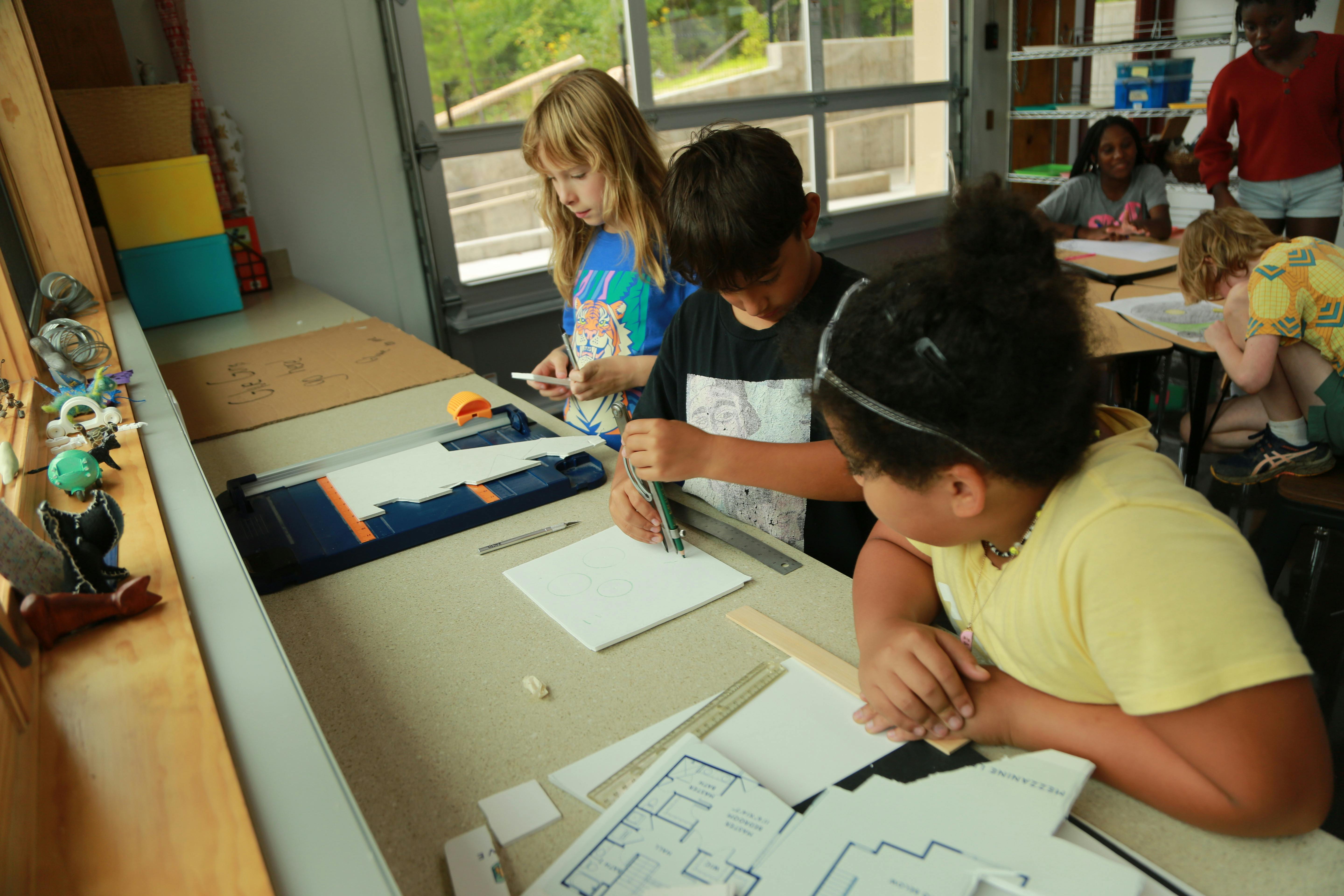 Three children working on projects at a table in a classroom