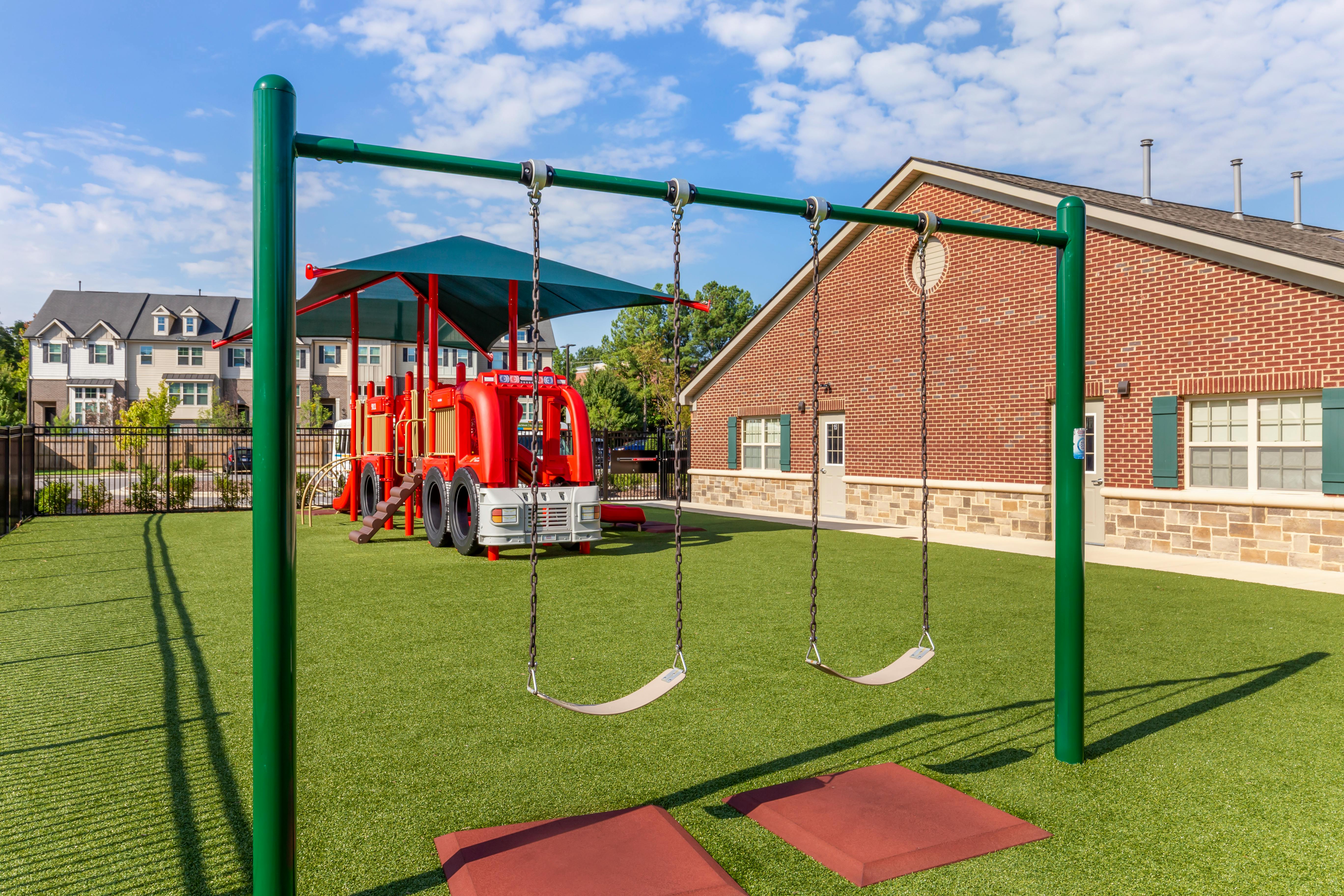 Swings and a red fire truck-shaped play structure on green artificial turf