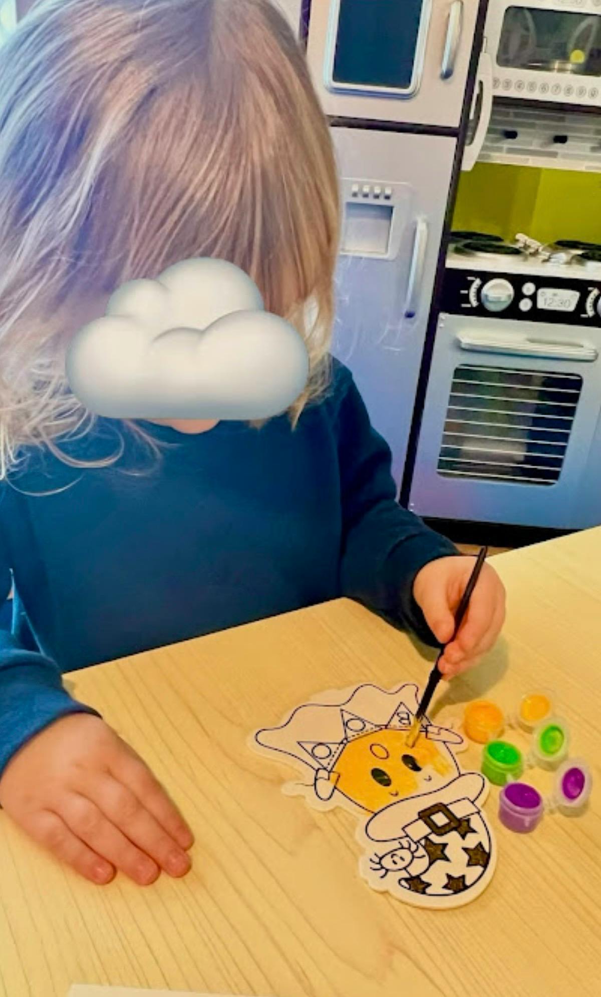 Child painting a cartoon cupcake with a brush and small paint pots