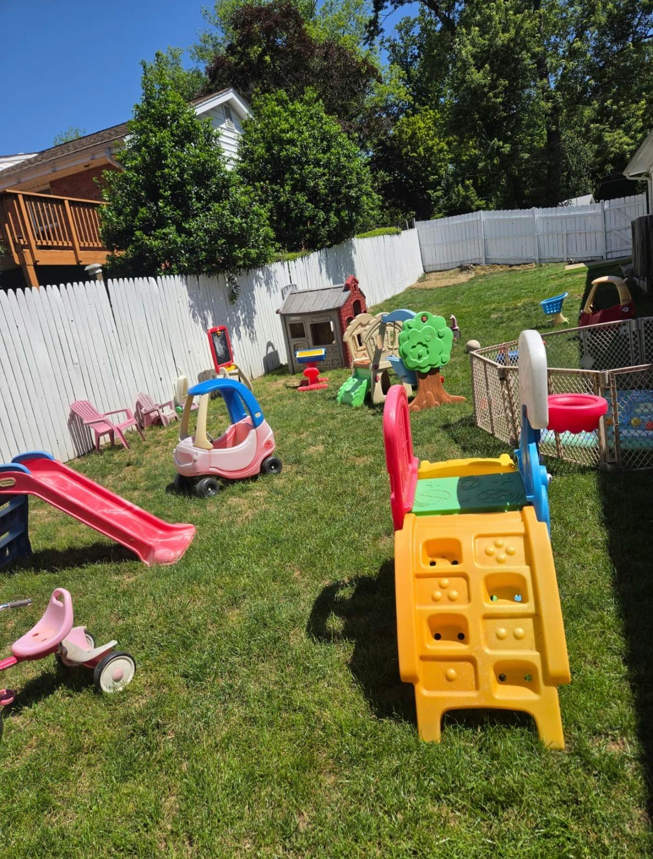 Plastic playground equipment and toys scattered across a grassy backyard