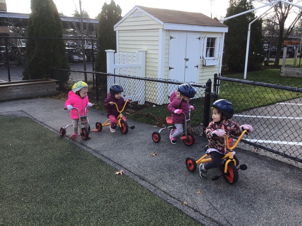 Four children wearing helmets riding tricycles on a paved path