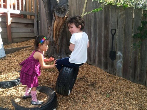 Two children playing with tires on wood chips
