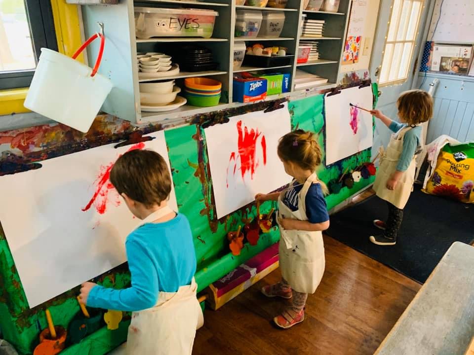 Three children painting on easels in a classroom