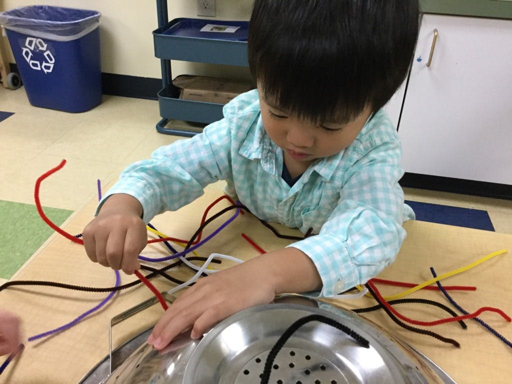 Child playing with pipe cleaners and a metal colander