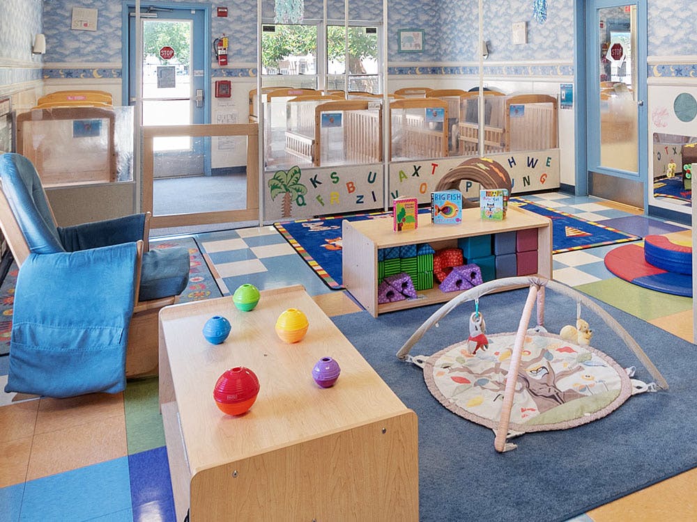 Baby room with multiple cribs, a blue rocking chair, and play mats