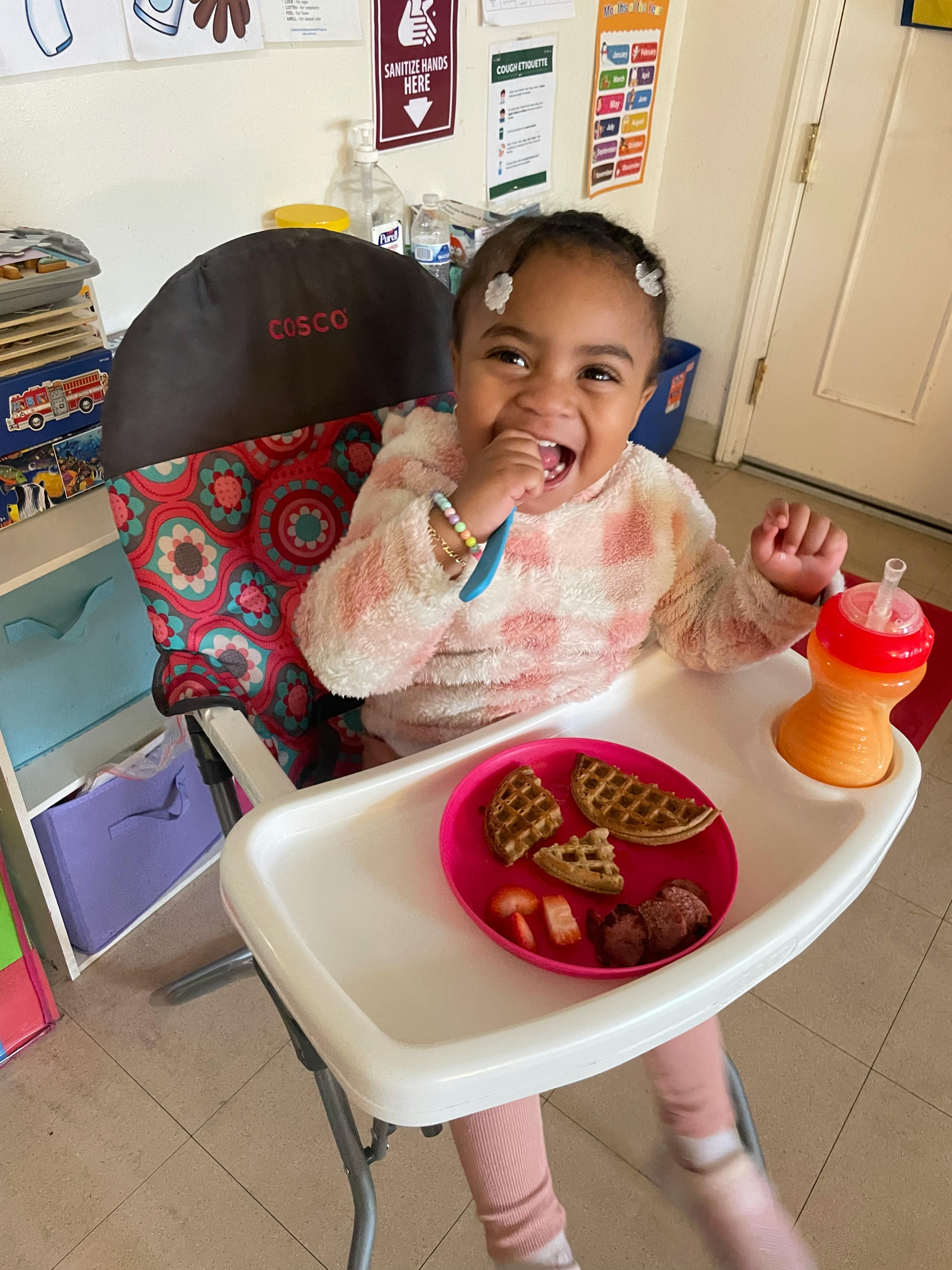 Child in a high chair with a plate of waffles and fruit