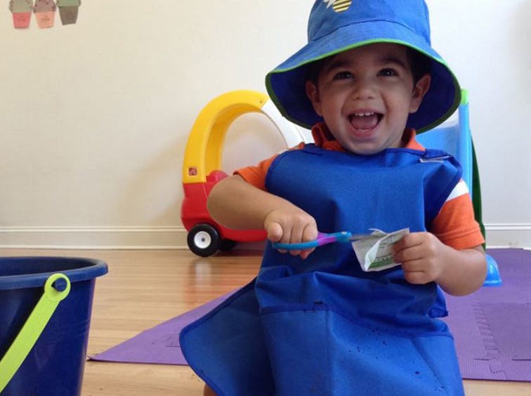 Child in a blue hat and apron cutting paper with scissors