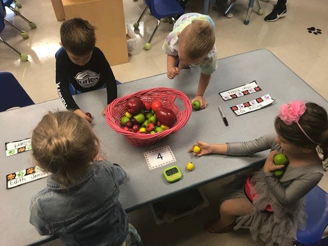 Children at a table with a basket of fruit and small objects