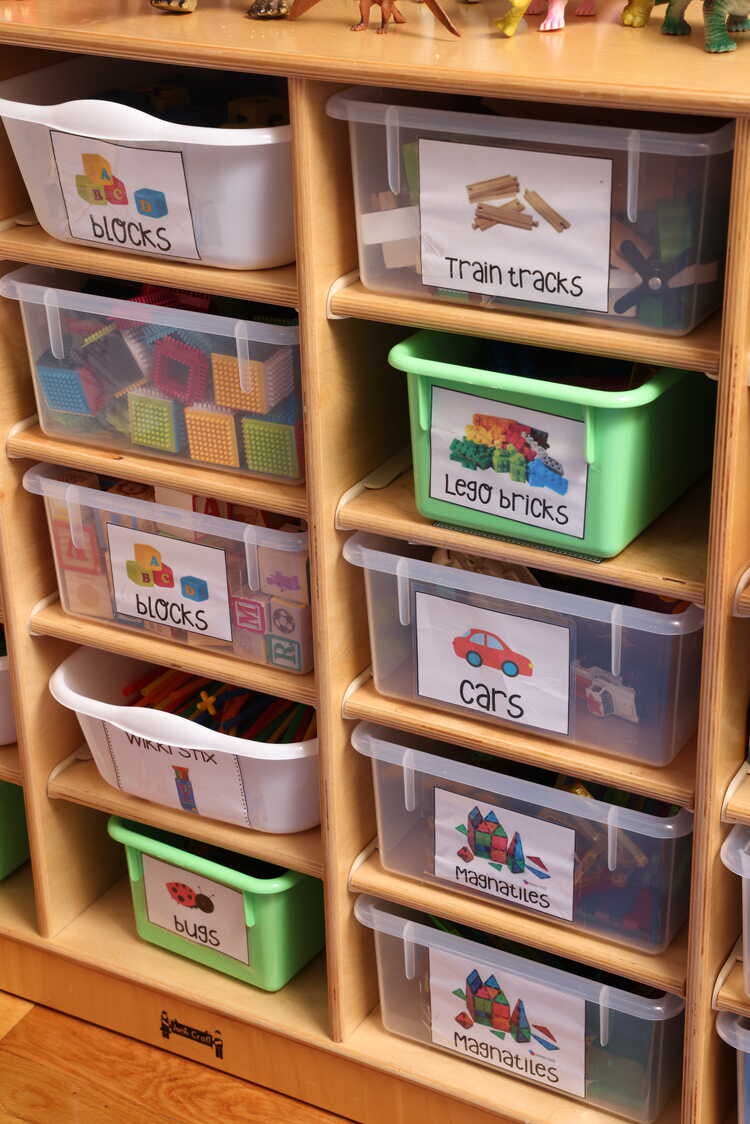 Shelves with labeled bins of toys including blocks, train tracks, Lego bricks, cars