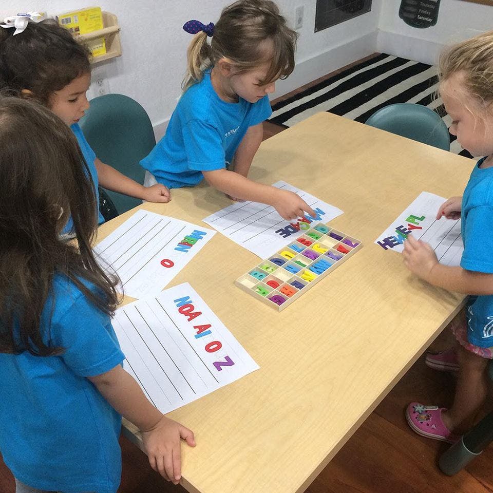 Children at a table with papers and colorful letter tiles