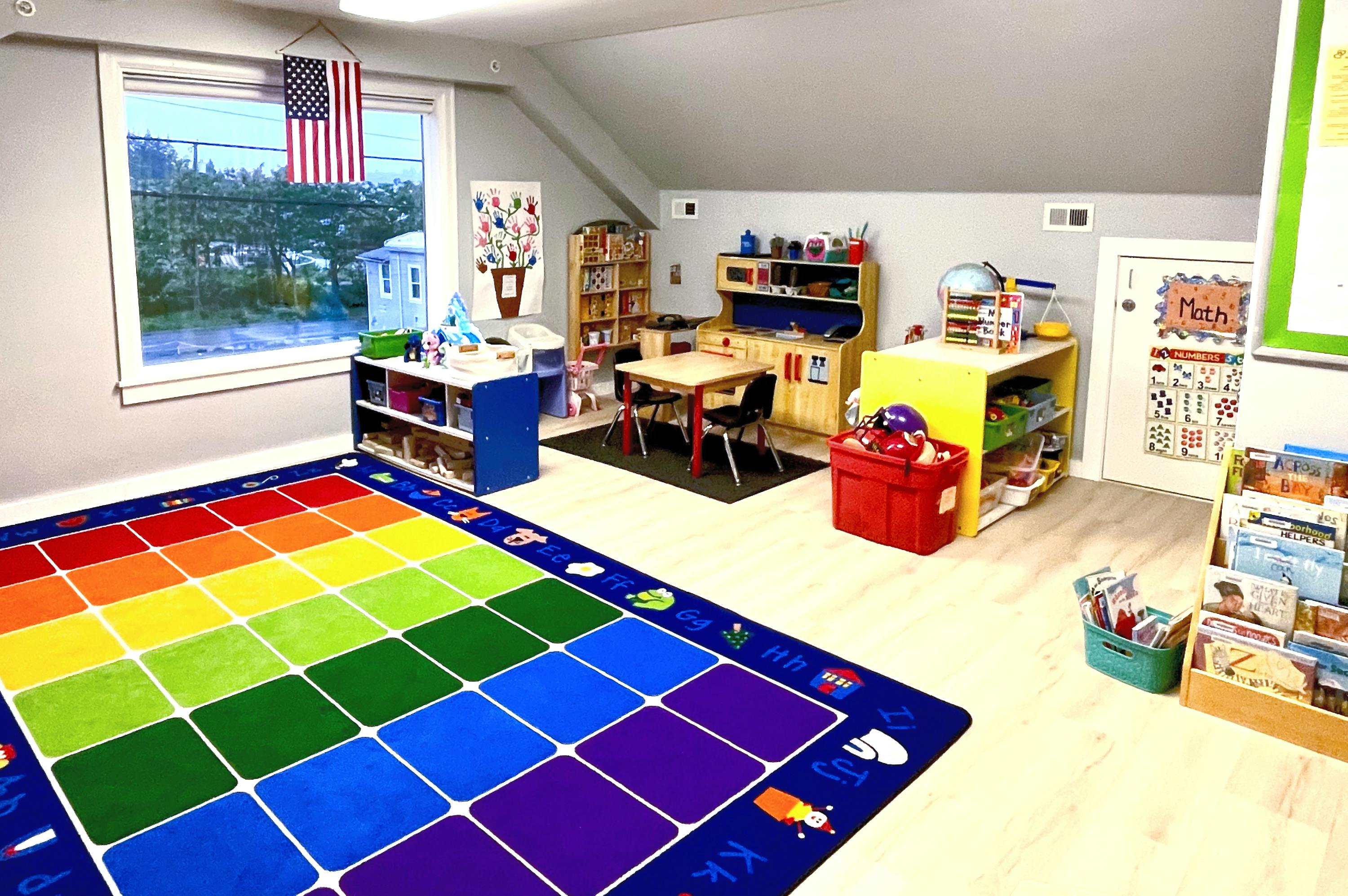 Classroom with a rainbow rug, small tables, and storage shelves
