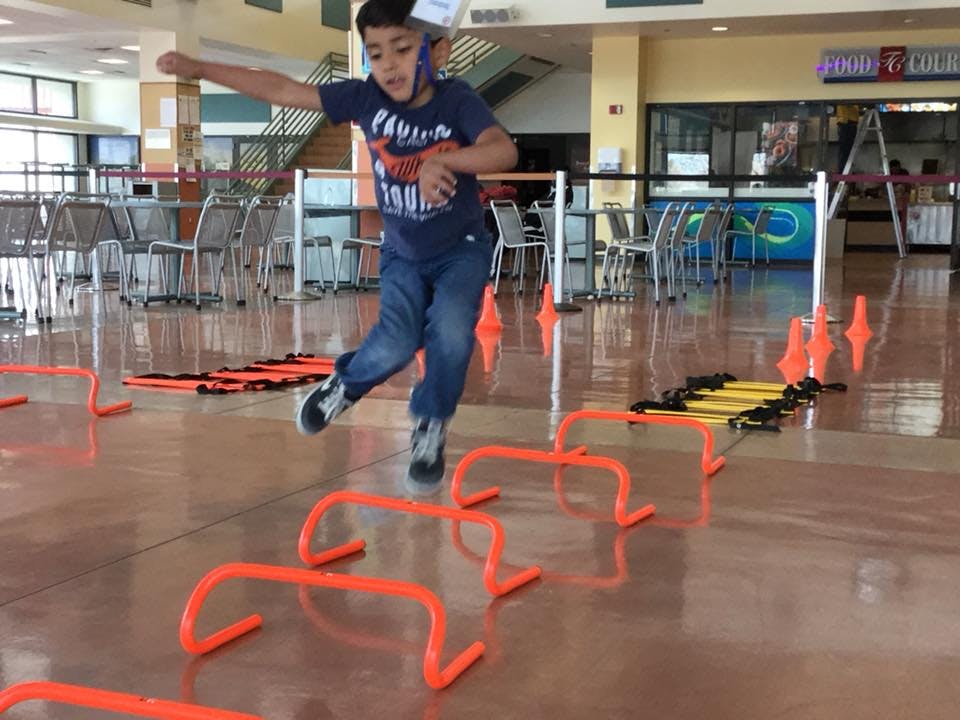 Child jumping over orange hurdles indoors