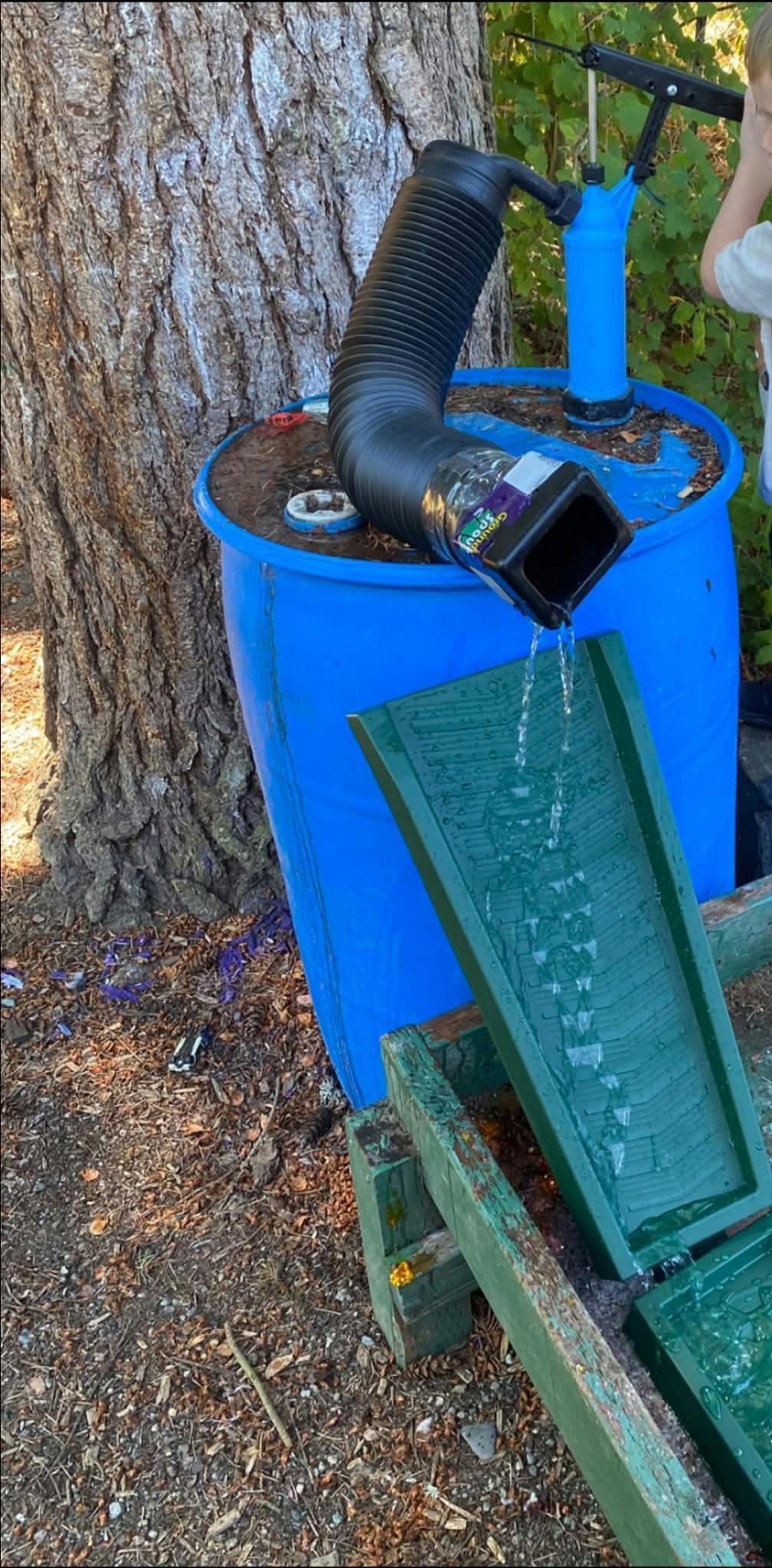 Water pumping from a blue barrel onto a green sluice box